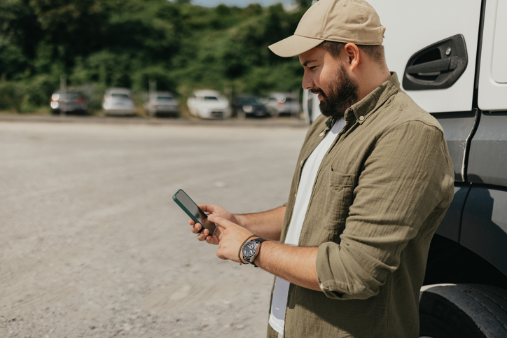 Motorista de caminhão sorridente com os braços cruzados ao lado de um veículo de carga branco estacionado